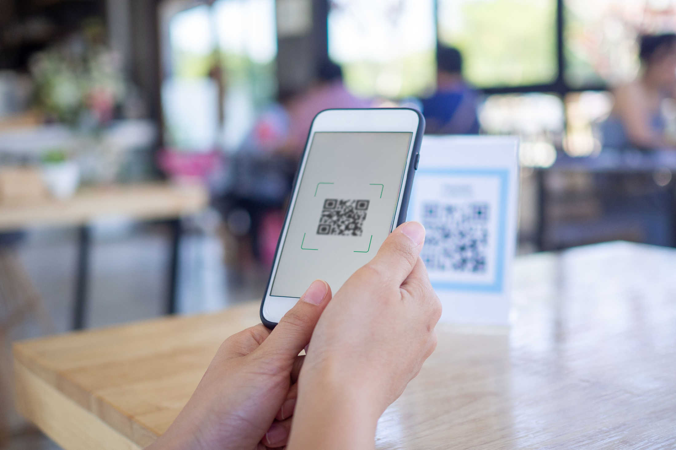 Female using digital transformation services to scan a QR code on her smartphone at a restaurant table to access the menu.
