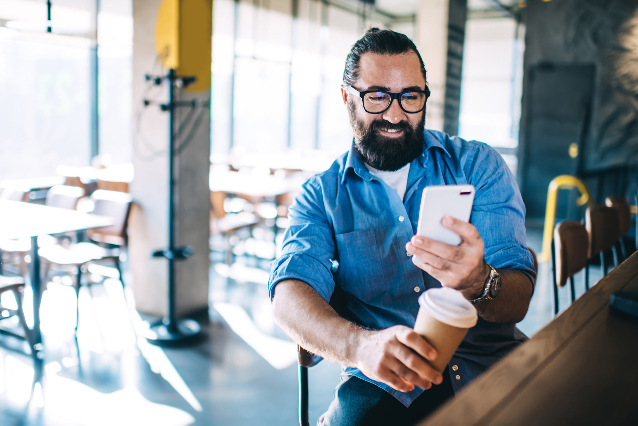 Bearded man sitting in a coffee shop with a smart phone.